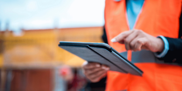 Mitarbeiter mit Warnweste auf Baustelle nutzt Tablet zur digitalen Bau- und Projektsteuerung