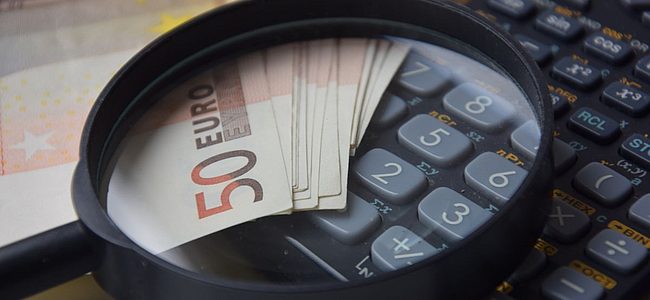 Lupe über 50-Euro-Scheinen und Taschenrechner, Symbol für Kostenanalyse oder Finanzprüfung